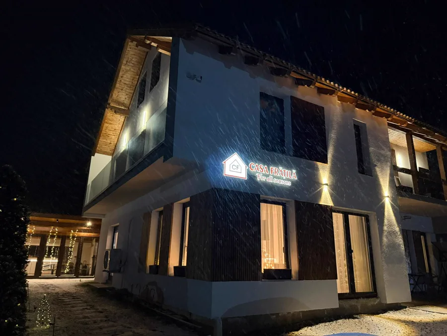 Casa Frătilă at night in snowfall — illuminated sign in the snow
